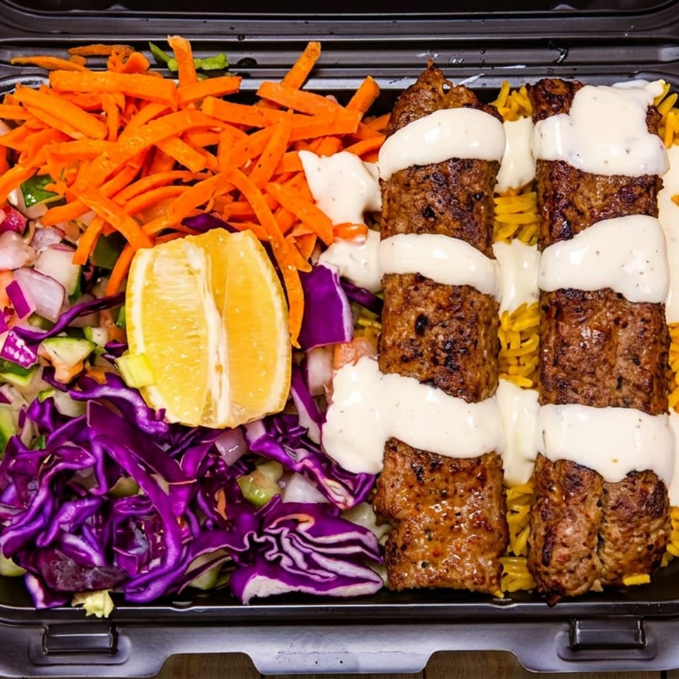 A takeout container filled with three kebabs drizzled with white sauce, yellow rice, shredded carrots, and salad.